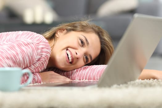 Happy woman laughing checking laptop on the floor at home