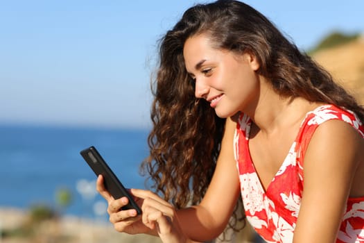 Happy tourist in red using smart phone on the beach on summer vacation