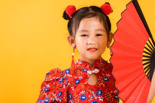 Chinese New Year. Happy Asian Chinese little girl smile wearing red cheongsam holding fan, Portrait children in traditional dress, studio short isolated on yellow background