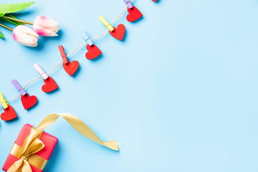 Happy Valentine's day concept. red heart-shaped valentines decoration hanging with clips for love and red gift box with golden ribbon on the rope greeting card on blue background with copy space