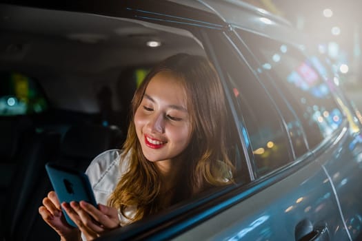 Asian businesswoman commuting from office in Taxi backseat with mobile phone on road in city at night after late work, Beautiful woman using smartphone sitting back seat her car in urban