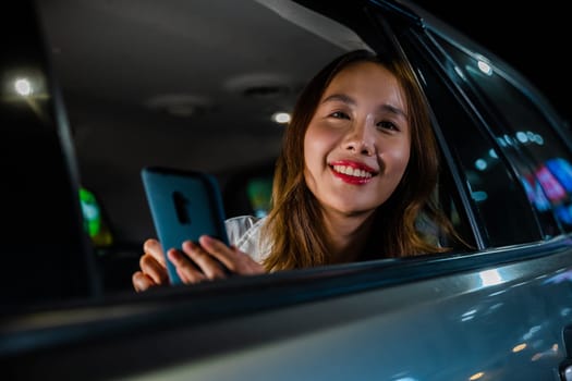 Happy beautiful woman texting smartphone sitting car back seat in urban, Asian businesswoman working late commuting from office in Taxi backseat with mobile phone in city at night after late work