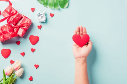 Valentine's day and birthday. Woman hands holding red heart and have gift or present box decorated surprise on blue background, Female's hand hold heart have gift box package in craft paper