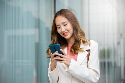 Happy business woman smiling using mobile phone outdoor walking on city street urban, Asian businesswoman texting smartphone commuting work she walking near her office building in morning