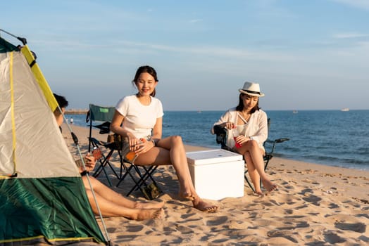 Happy friends with drinks in camp and laughing together in holidays on sand beach near camping tent vacation time at sunset, Young Asian group woman and man in summer travel outdoor