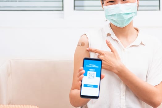 Asian young woman pointing to adhesive plaster on arm her vaccinated and showing app smartphone mobile digital screen vaccinated coronavirus (COVID-19) certificate after getting vaccine to prevent