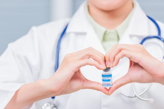 Closeup woman doctor smile forming a heart with her hands mark heart finger showing a glass vial of coronavirus vaccine, COVID-19 Medicine And Health Care Concept