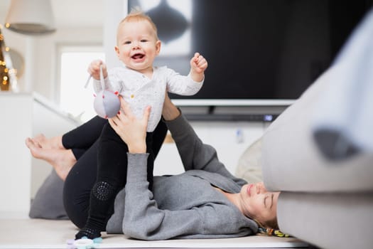Happy family moments. Mother lying comfortably on children's mat playing with her baby boy watching and suppervising his first steps. Positive human emotions, feelings, joy