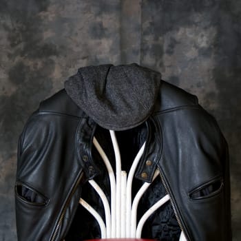A leather biker jacket hangs on the back of a chair with a tweed cap sitting on top.