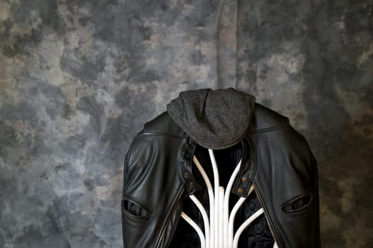 A leather motorcycle jacket hangs on the back of a chair with a tweed cap sitting on top.