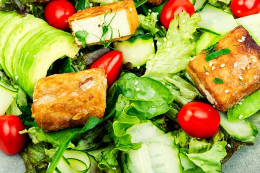 Appetizing lettuce salad, cucumber, avocado and breaded fried tofu soy cheese. Healthy eating, food background