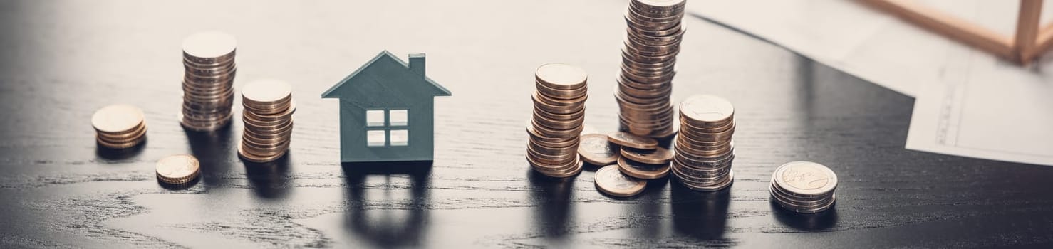 Model of a house and stacks of the coins on the black table. Concept of the planning for buying and ownership by appartment, building and renting.