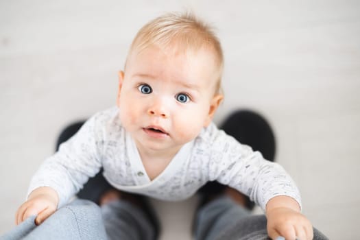 Top down view of cheerful baby boy infant taking first steps holding to father's sweatpants at home. Cute baby boy learning to walk.