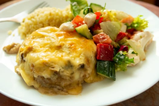 Dinner dish with large minced cutlet with yellow cheese and salad with red peppers, cucumber and white cheese.