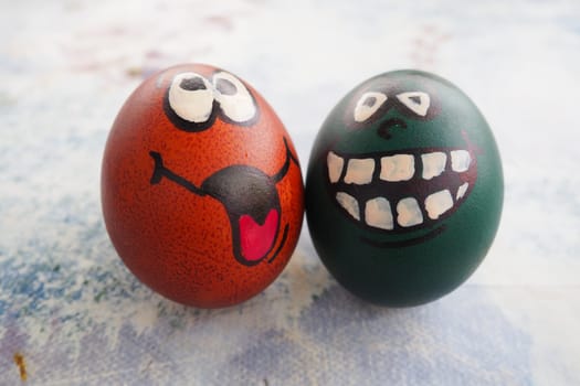 Easter eggs dyed green and brown with painted laughing faces. Funny grimaces with eyes, tongue and big white teeth. Scary face for Halloween. Emoticon for Easter. Light abstract background