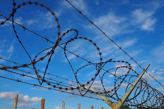 Barbed wire against the blue sky. Barbed wire is a wire or a narrow strip of metal with sharp spikes. Device of barriers. The concept of freedom, protection of property, violence, imprisonment.