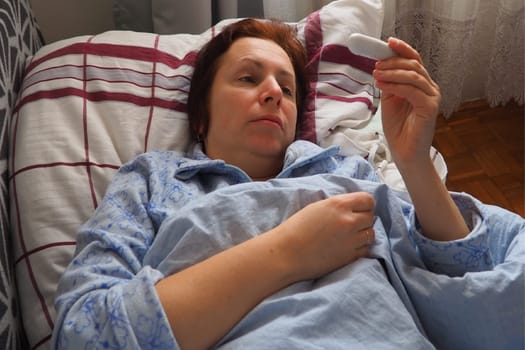 Sick woman in bed. Headache, runny nose and cold. Paleness of the face and faintness of the body. Feeling unwell. The patient lies on a pillow, holds a thermometer and measures the temperature