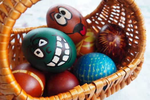 Easter eggs painted in different colors with painted laughing faces. Funny grimaces with eyes tongue and big white teeth. Scary face for Halloween. Emoticon for Easter Wicker basket. White background