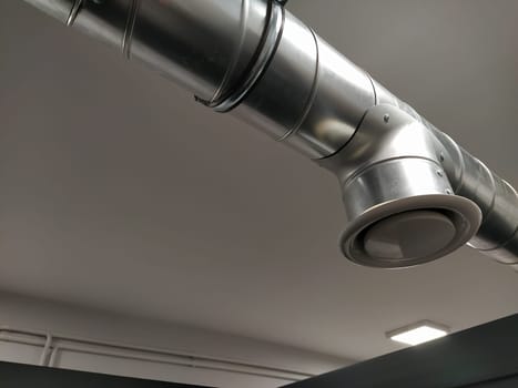 Extractor hood in a public toilet. Round metal pipe with gray air extractor. Engineering ventilation systems. Galvanized pipes under the ceiling of the room. Plastic round tip.