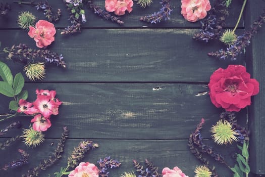 Flowers in a circle on a wooden background. Postcard for the holiday. Roses, geraniums, lavender, sage and hairy chestnuts are placed along the edges on dark boards. Background copy space, flat lay
