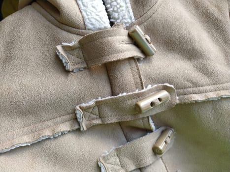 Suede outerwear. Overhead loops for buttons. Hidden zipper. Beige faux suede with sheepskin on the fold of a demi-season garment. seams in the material. Clothing industry and fashion