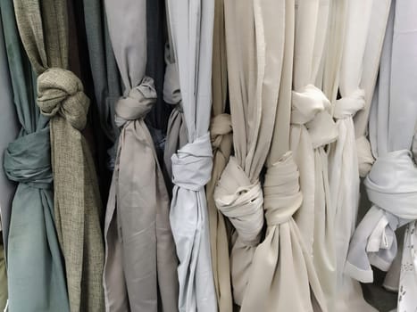 Curtain and fabric for drapery and interior decoration. Samples of gray and white fabrics in the store are hung vertically and tied in knots. Curtains in the showcase