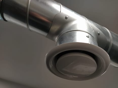 Extractor hood in a public toilet. Round metal pipe with gray air extractor. Engineering ventilation systems. Galvanized pipes under the ceiling of the room. Plastic round tip.