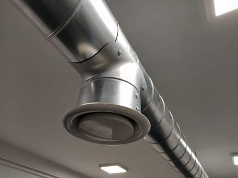 Extractor hood in a public toilet. Round metal pipe with gray air extractor. Engineering ventilation systems. Galvanized pipes under the ceiling of the room. Plastic round tip.