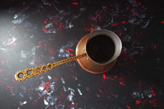 Balkan cezve for turkish coffee. A copper cezve on black surface. Antique bronze utensils. Carved metal handle with pattern. Black background with white, red and blue spots