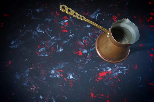 Balkan cezve for turkish coffee. A copper cezve on black surface. Antique bronze utensils. Carved metal handle with pattern. Black background with white, red and blue spots