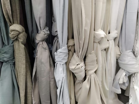 Curtain and fabric for drapery and interior decoration. Samples of gray and white fabrics in the store are hung vertically and tied in knots. Curtains in the showcase.