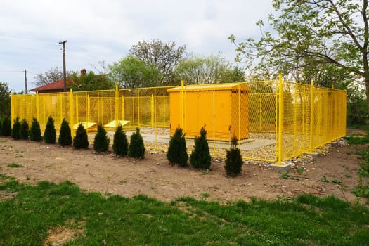 ground with tanks for liquefied gas. Modern gas installation with protective fencing. Yellow fence. Supply of gas to population. Connection of houses to energy. Gas and energy prices. Planted thuja.