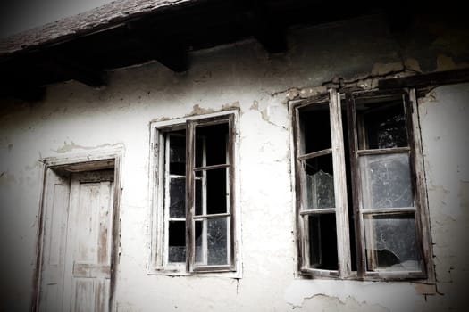 Abandoned spooky old house. Wooden windows and doors. The hut is a mud hut. Samani house. White stucco plaster. Halloween theme. Aging, loneliness, departure, war and devastation. Ukraine, Donbass.