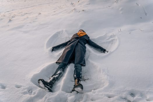 A woman lies in the snow in the shape of a snow angel in winter.
