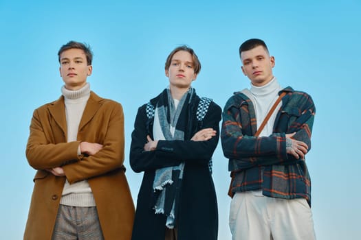 Three young men in autumn clothes are standing with crossed hands on the street