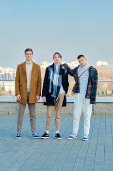 Three young men in autumn clothes are walking down the street