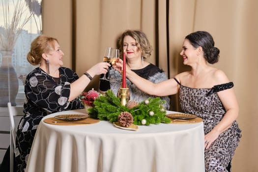 Three juyful middle age women celebrating christmas sitting behind the festive table
