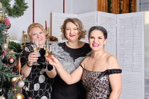 Three joyful middle age women celebrating christmas standing near christmas tree