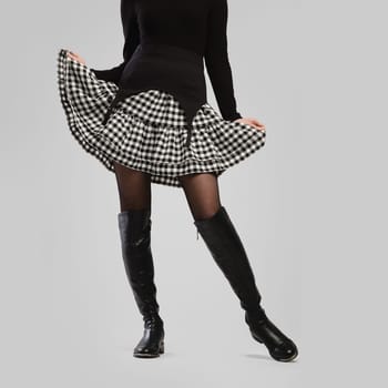Slender female legs in tall boots and little skirt over grey background