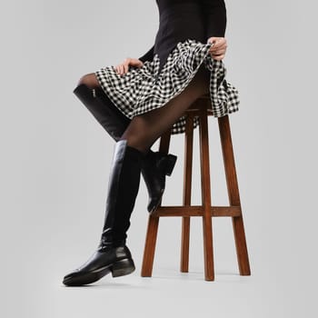 Slender female legs in tall boots and little skirt over grey background