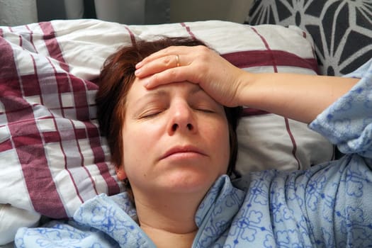 Sick woman in bed. Headache, runny nose and cold. Paleness of the face and faintness of the body. Feeling unwell. The patient holds his forehead with his hand and covers his eyes.