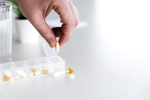 Closeup of female elderly hand taking medicine from medical pill box, sorting pills. Tablet doses for daily take with different drugs and capsules. Young woman getting her daily vitamins at home