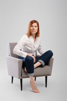 Middle age woman sitting in armchair and looking tense. Studio concept of carefree life.