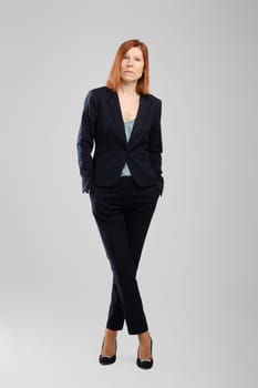 Stylish middle aged woman in pantsuit standing in studio over grey background