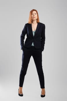 Stylish middle aged woman in pantsuit posing in studio over grey background