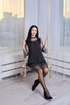 Pretty young woman having fun at home, swinging on swing.
