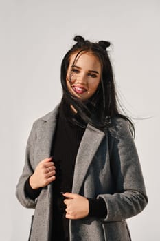 Young woman posing in warm coat with white wall on background in windy day