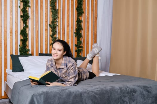 Clever young woman reading the book in bed during vacation