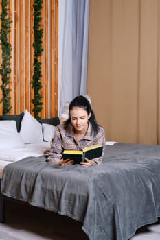 Clever young woman reading the book in bed during vacation