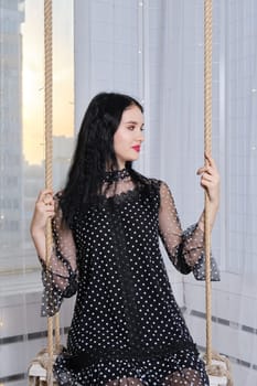 Pretty young woman having fun at home, swinging on swing.